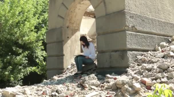 Hermosa morena está leyendo un libro sentado en las ruinas de un edificio . — Vídeo de stock