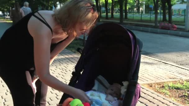 Mamma gioca con il bambino sdraiato in una carrozzina su una passeggiata . — Video Stock