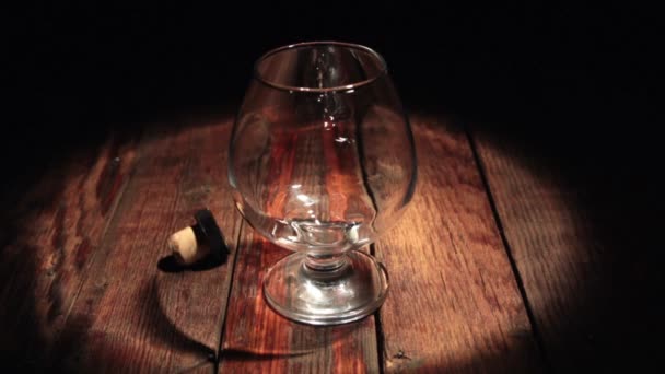 Pouring cognac from the bottle on black background in the beam of light. — Stock Video