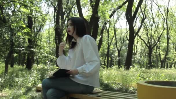 Chica se sienta y lee un libro en el parque . — Vídeos de Stock
