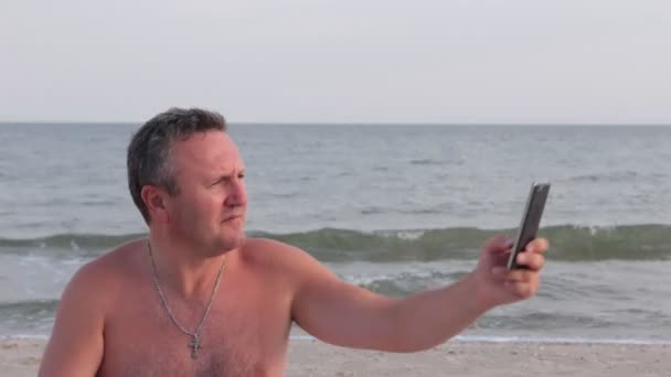 L'uomo fa selfie sulla spiaggia sullo sfondo delle onde . — Video Stock