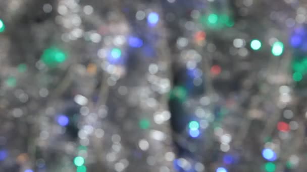 Wind blowing on defocused silver tinsel and a garland of colored lights. — Stock Video