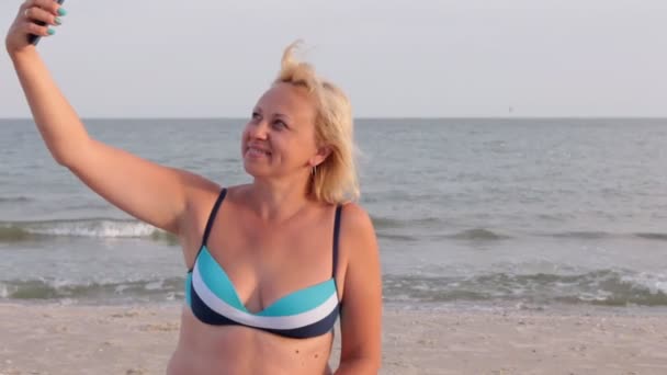 Mulher faz selfie na praia contra o pano de fundo das ondas . — Vídeo de Stock