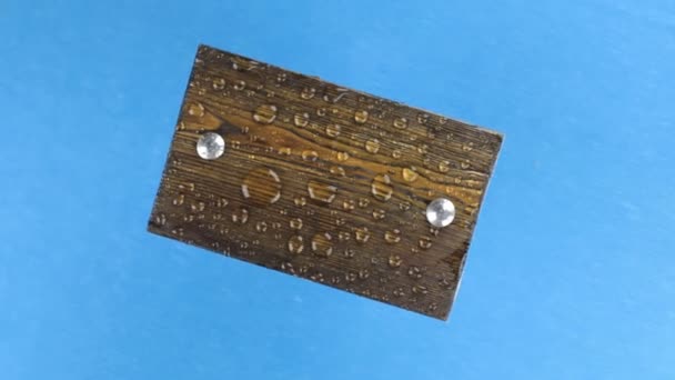 Vento treme gotas de água em uma placa de madeira rotativa com parafusos de ferro, isolado em azul . — Vídeo de Stock