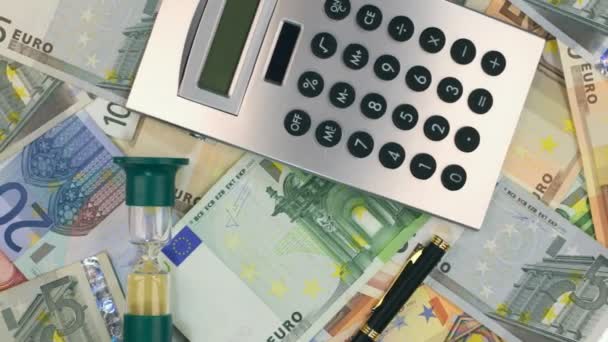 Drehung der Sanduhr und des Taschenrechners, Stift auf dem Euro liegend. Ansicht von oben. — Stockvideo