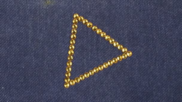 Rotatie van een driehoek gemaakt van gele steentjes op denim, de driehoek symboliseert voltooiing. — Stockvideo