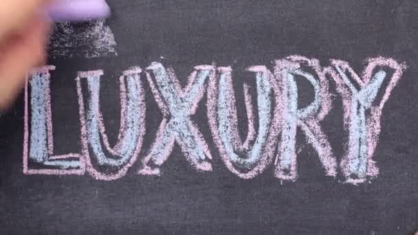 Word LUXURY, written by hand in chalk on a blackboard. — Stock Video