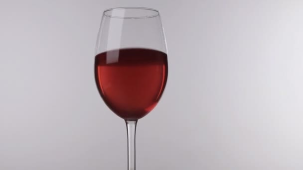 Movimiento del vino tinto en una copa de pie sobre un fondo blanco, primer plano . — Vídeo de stock