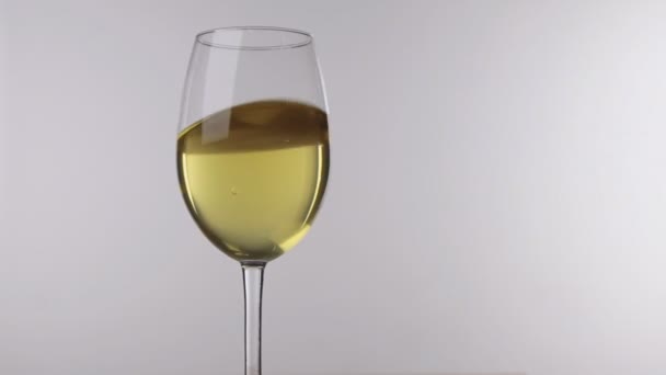 Movimiento del vino blanco en una copa de pie sobre un fondo blanco, primer plano . — Vídeos de Stock