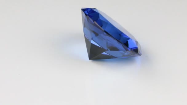 Gire de un gran rhinestone azul sobre un fondo blanco. Hermoso reflejo de luz de una textura de diamante . — Vídeo de stock