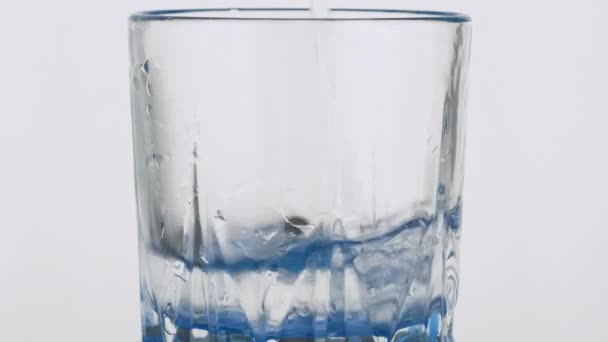 Zeitlupe. Reines Wasser, das in einen Glasbecher auf weißem Hintergrund gegossen wird. — Stockvideo
