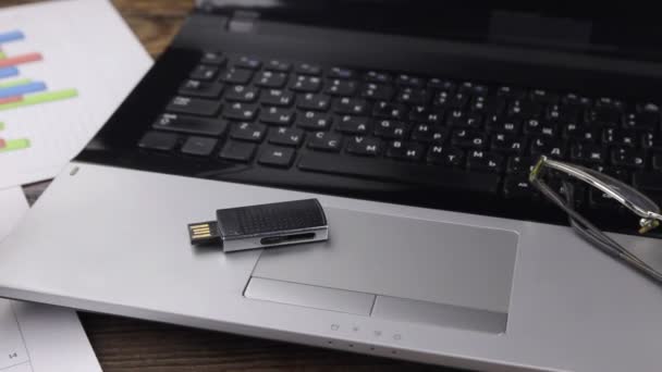 Primer plano. Unidad flash USB y gafas tumbadas en un ordenador portátil. — Vídeos de Stock