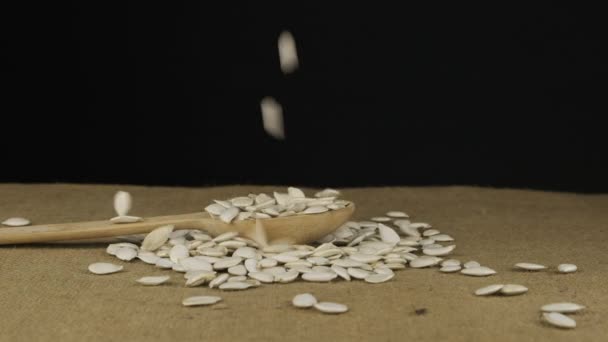 Pompoenkorrels vallen in een houten lepel en de hoop wordt gegoten. Langzame beweging. — Stockvideo