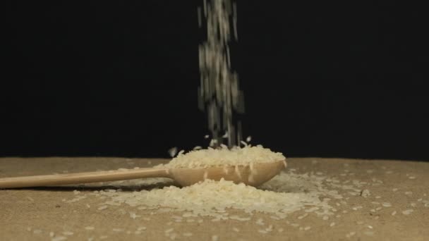 Rice grains fall into a wooden spoon and heap is poured. Slow motion. — Stock Video