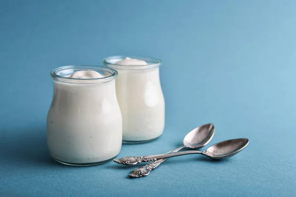 希腊酸奶在一个玻璃罐子与勺子在蓝色背景特写 — 图库照片
