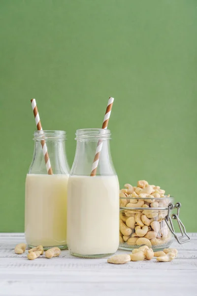 Två Flaskor Vegetarisk Cashew Mjölk Med Cashewnötter Grön Bakgrund — Stockfoto