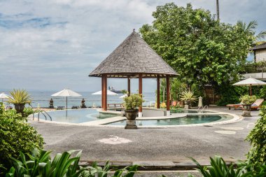 BALI, INDONESIA - JANUARY 14, 2018: Territory Discovery Candidasa Cottages and Villas Hotel with swimming pool and sea view at sunny day, Bali, Indonesia clipart
