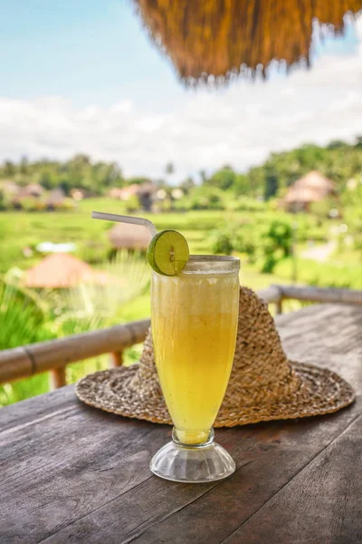 Pineapple juice and straw hat on wooden table — Stock Photo, Image