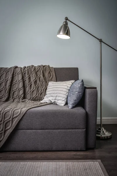 蓝色墙壁的房间里有靠垫 针织格子布和落地灯的灰色沙发 — 图库照片