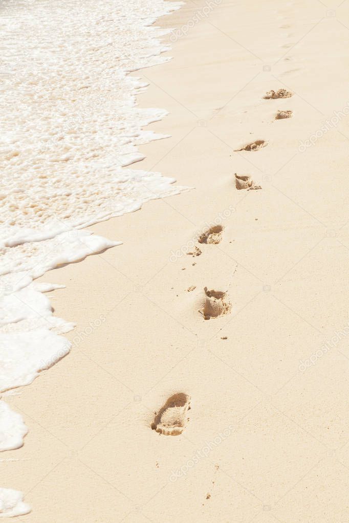 Imprint of human feet on the beach sand near the water shore 