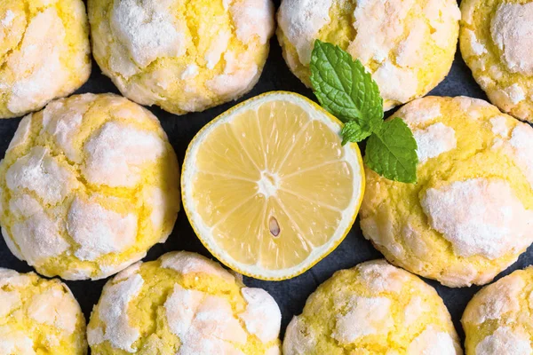 Background of freshly backed cracked crinkle Lemon cookies and slice of fresh lemon on dark background. Close up. Top view