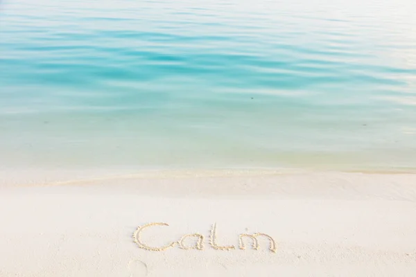 背景が青い海のビーチで砂で書かれた単語穏やかです — ストック写真