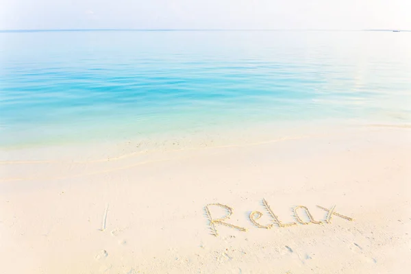単語リラックス朝海背景でビーチの砂で書かれて — ストック写真
