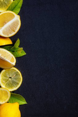 Taze kesilmiş ve bütün limon yeşil yapraklar koyu taş masanın üstünde. Kopya alanı ile yeşil yaprakları ile üst görünümden olgun limon