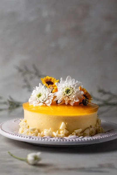 Mango cheesecake with yellow jelly topping, with flowers and fresh mango pieces on grey background , vertical composition