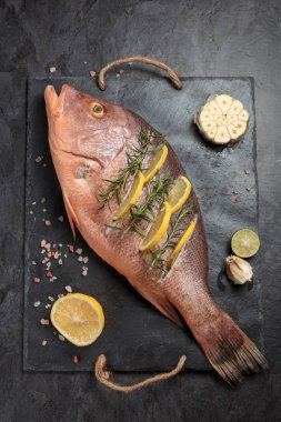 Taze limon dilimleri, sarımsak ve biberiye otlar, koyu arka plan, üstten görünüm üzerinde ham Red snapper balıkla Marine. Dikey kompozisyon  