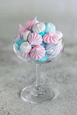 Ev yapımı pastel pembe, mavi ve beyaz beze cam nötr gri arka plan üzerinde. Dikey minimalist kompozisyon 