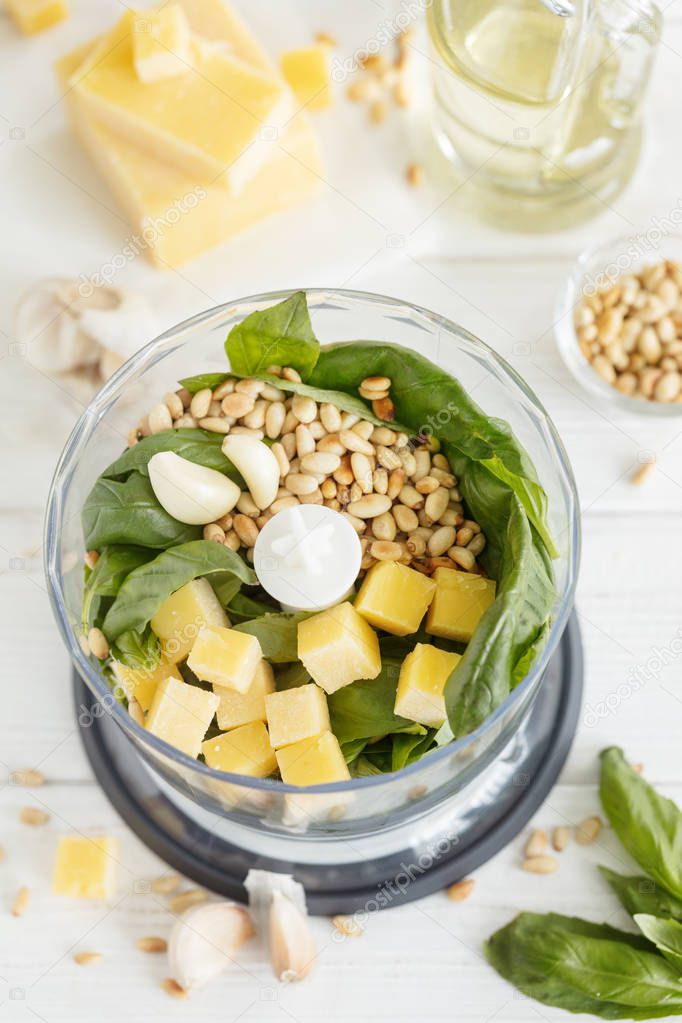 Ingredients for Basil pesto sauce in mixing blender bowl on white background, vertical composition