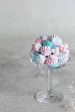 Ev yapımı pastel pembe, mavi ve beyaz beze cam nötr gri arka plan üzerinde. Dikey minimalist kompozisyon 