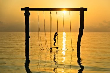 Ma günbatımı deniz manzarası üzerinde ip salıncak üzerinde genç çocuk silüeti