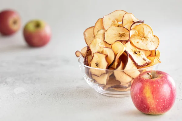 Hipped Dried apple chips in glass bowl with fresh apple in foreground on light background - Image — Stock Photo, Image