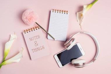 Pembe kulaklık, telefon, boş not defteri ve pembe backgro üzerinde kalem