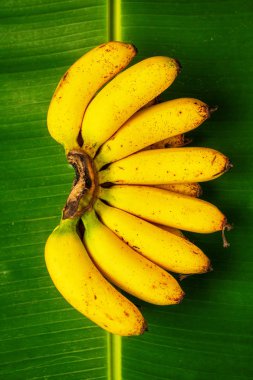 Bunch of fresh bananas on banana leaves, top view, vertical comp clipart