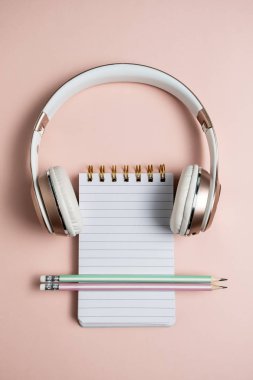 Pembe kulaklık, boş açık not defteri ve pembe backgroun üzerinde kalemler