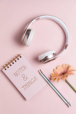 Pembe arka plan üzerinde pembe kulaklık, not defteri, çiçek ve kalemler, 