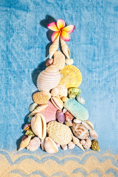 Christmas background with a creative arrangement of seashells, corals and white frangipani flower forming a Xmas tree on blue background, flat lay, vertical composition — Stock Photo, Image