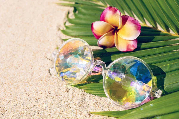 Divertenti caleidoscopio occhiali rosa su sfondo sabbia con ramo di palma, spazio copia, posa piatta — Foto Stock