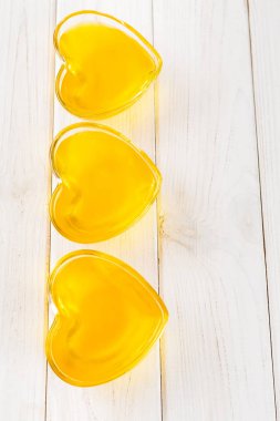 Beyaz ahşap arka plan üzerinde kalp şeklinde cam sarı limon jöle, üst görünümü