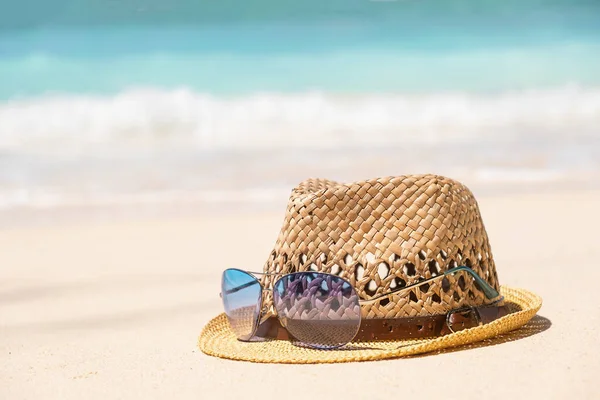 青い海の水と砂の背景を持つ海辺の海岸で夏の帽子と青いサングラス 夏の熱帯の休日のコンセプト — ストック写真