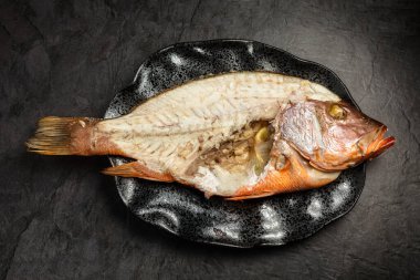 Yarı çıplak kemikli, kırmızı balık yiyen, koyu arka planda, üst manzaralı.