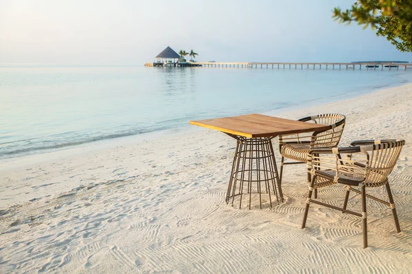 早朝の熱帯海岸の水による熱帯ビーチの木製のテーブルと椅子 率直な光 — ストック写真