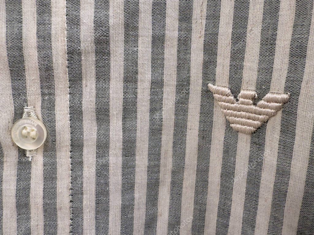 Singapore, Singapore - May 03, 2025 Close-up of an Armani striped shirt showcasing a button and embroidered logo, highlighting the fabric texture and craftsmanship in fashion design