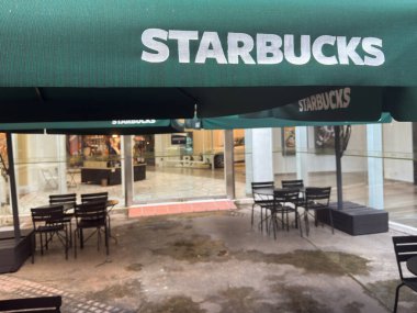 Penang, Malezya - 7 Temmuz 2025: Starbucks 'ta açık hava oturma alanı yeşil şemsiyelerin altında birçok siyah sandalye ve masa ve arka planda bir alışveriş merkezi görünür..