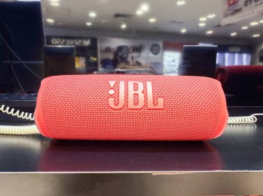Penang, Malezya - 7 Temmuz 2025: Perakende satış tezgahına kırmızı bir JBL hoparlörü yerleştirilir, desenli yüzeyi gösterilir ve sergilenmek için sarmal bir kabloyla markalaştırılır..