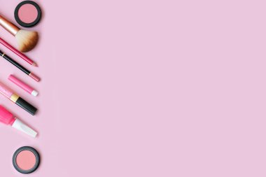 Pembe arka planda boş fotokopi alanı olan kozmetik ürünler. Makyaj, pastel renkli arka planlı cilt bakımı konsepti. Allık, dudak parlatıcısı, dudak kalemi, göz farı, oje, parfüm ve fırça..