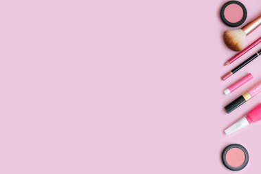 Pembe arka planda boş fotokopi alanı olan kozmetik ürünler. Makyaj, pastel renkli arka planlı cilt bakımı konsepti. Allık, dudak parlatıcısı, dudak kalemi, göz farı, oje, parfüm ve fırça..